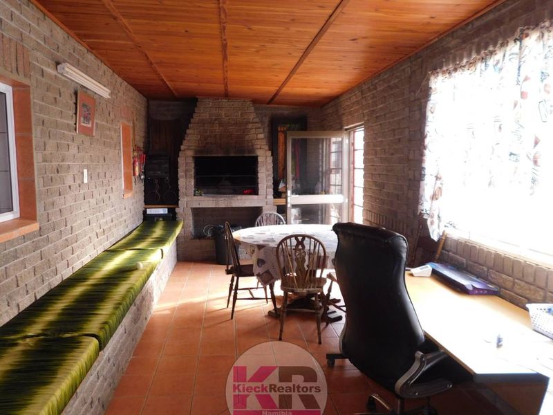 A covered patio area featuring exposed brick walls, a timber ceiling, tiled flooring, and a built-in braai, suitable for outdoor entertaining.