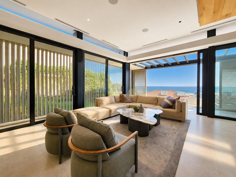 Modern, light-filled living room featuring floor-to-ceiling glass doors, recessed lighting, and seamless indoor-outdoor flow with expansive ocean views.