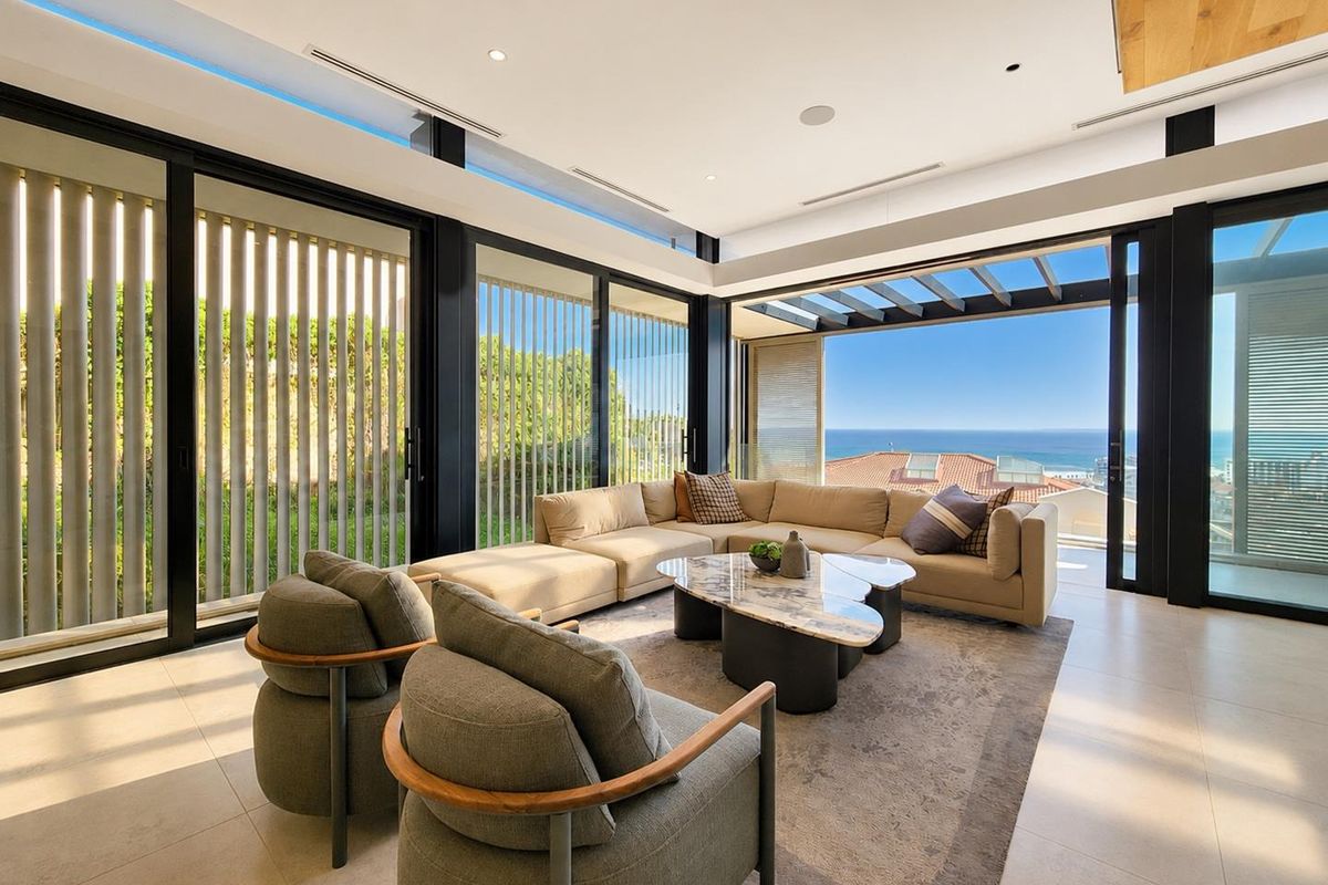 Modern, light-filled living room featuring floor-to-ceiling glass doors, recessed lighting, and seamless indoor-outdoor flow with expansive ocean views.