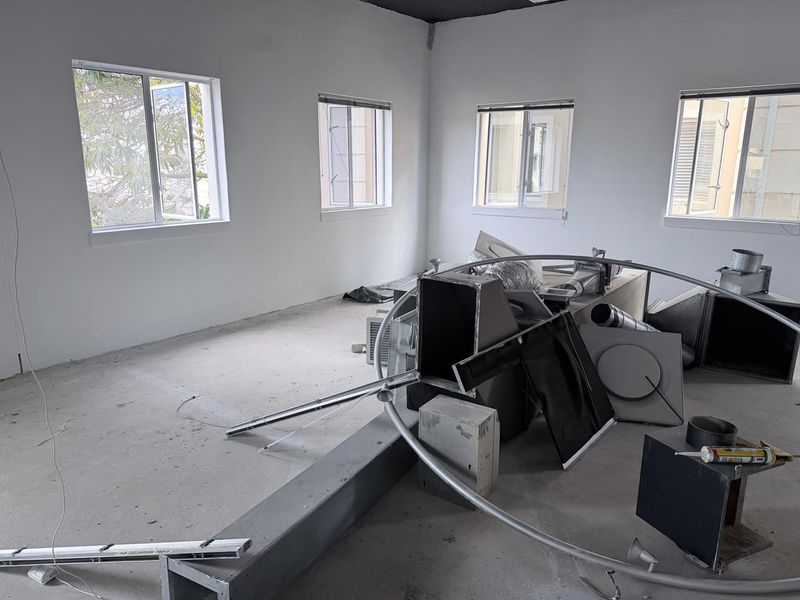 An unfinished office space featuring concrete flooring, multiple casement windows, and exposed HVAC ductwork, currently undergoing renovation or fit-out.