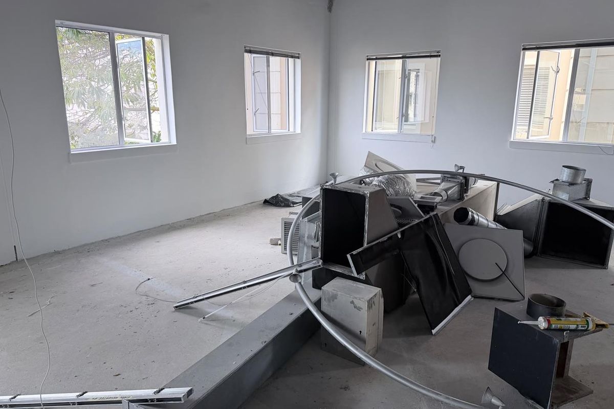 An unfinished office space featuring concrete flooring, multiple casement windows, and exposed HVAC ductwork, currently undergoing renovation or fit-out.