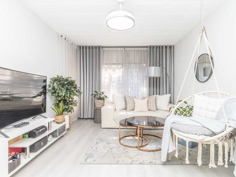 A bright and well-maintained living room featuring neutral tones, laminate flooring, and floor-to-ceiling window treatments.