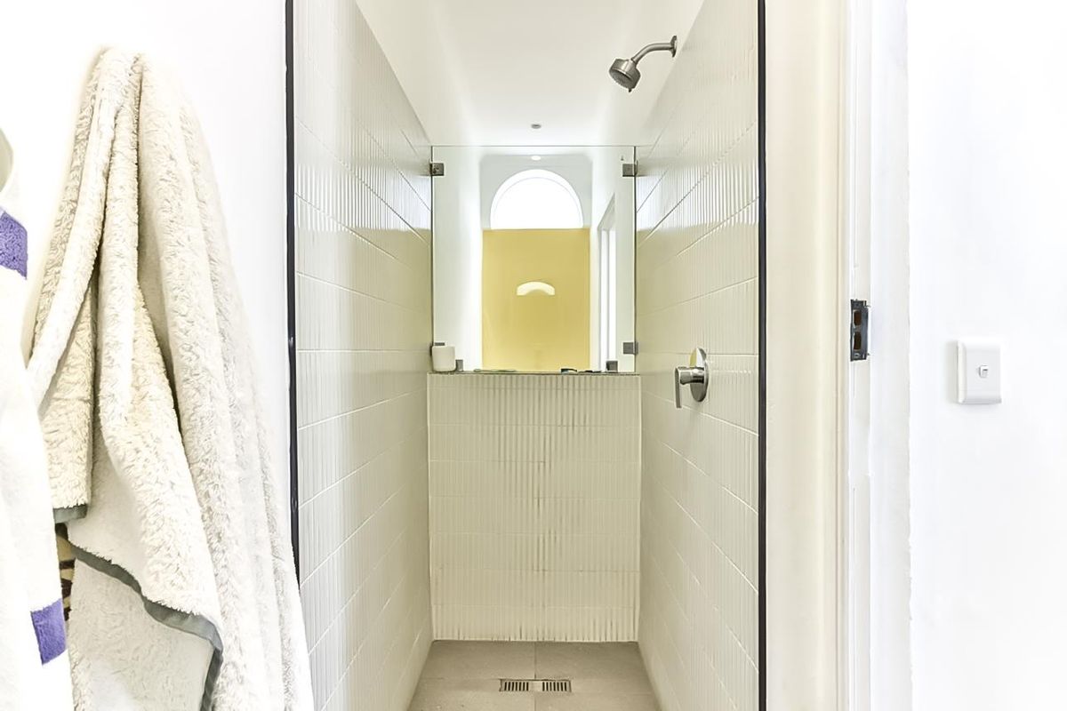 A clean, modern walk-in shower featuring white vertical tiled walls, a linear floor drain, and a large mirror reflecting the adjacent space.