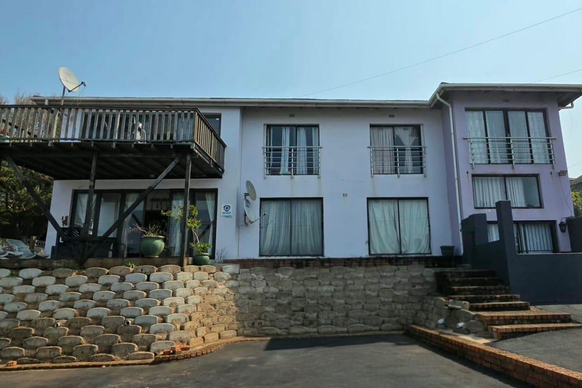 Rear elevation of a multi-story house featuring a raised wooden deck, retaining wall, and paved driveway area.