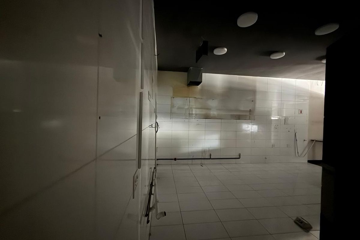 An empty commercial kitchen space featuring white tiled walls, tiled flooring, and a dark ceiling, suitable for a custom retail or food service fit-out.