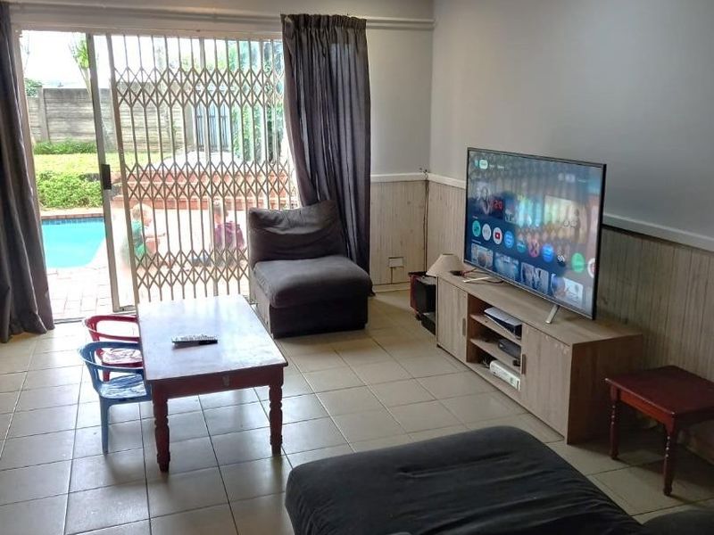 A living room featuring tiled floors, timber wall paneling, and a sliding glass door providing direct access to the outdoor pool area.