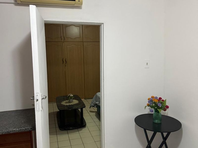 A bedroom featuring built-in wooden cupboards, tiled flooring, and a wall-mounted air conditioning unit, viewed from an adjacent tiled space.