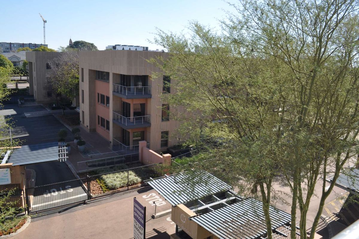 An elevated aerial view of the apartment complex exterior, featuring balconies, paved driveway access, and landscaped garden areas.