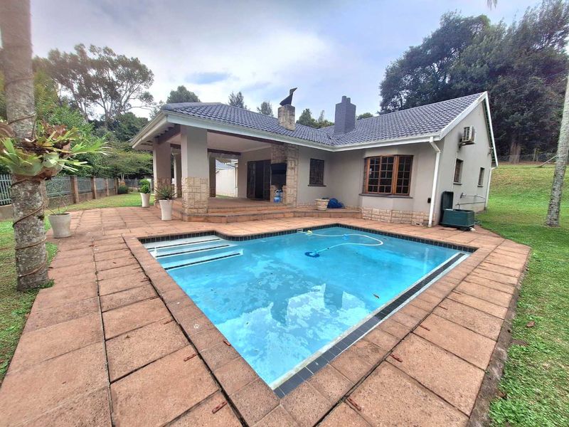 Rear exterior view featuring a swimming pool, a covered patio area with stone detailing, and a well-maintained garden setting.