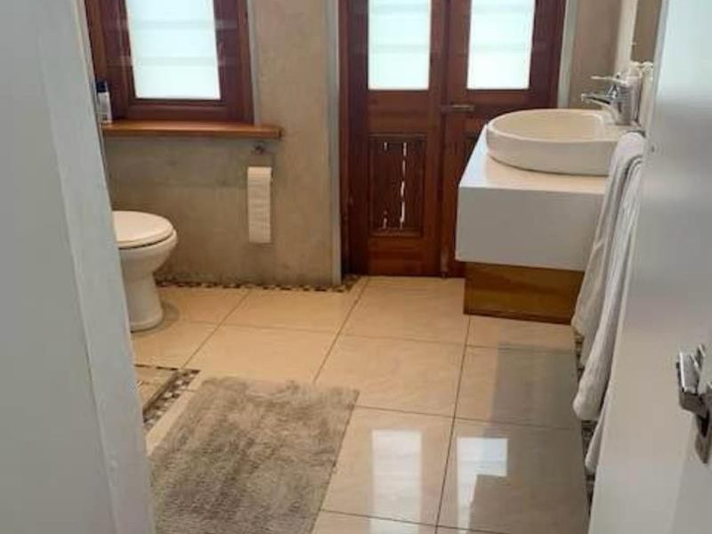A bathroom featuring a vessel sink on a wall-mounted vanity, tiled flooring with mosaic accents, and wooden door and window frames.