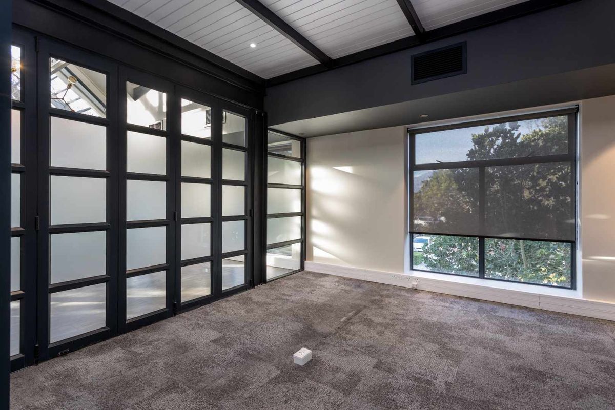 A modern, empty office space featuring dark-framed glass partitions, carpeted flooring, and large windows that provide ample natural light.