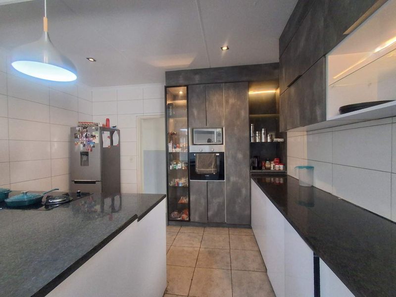 Modern kitchen featuring dark cabinetry, granite countertops, built-in oven and microwave, gas hob, and tiled flooring.