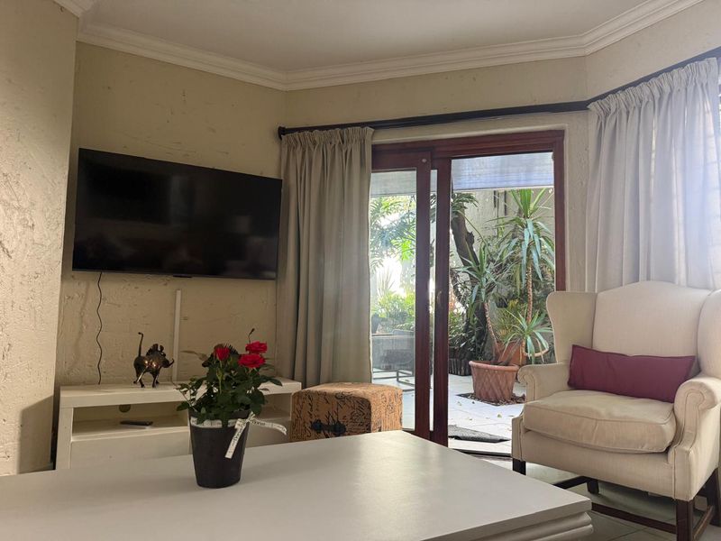 A living room featuring tiled floors, cove cornicing, and a sliding glass door providing direct access to a private garden patio area.