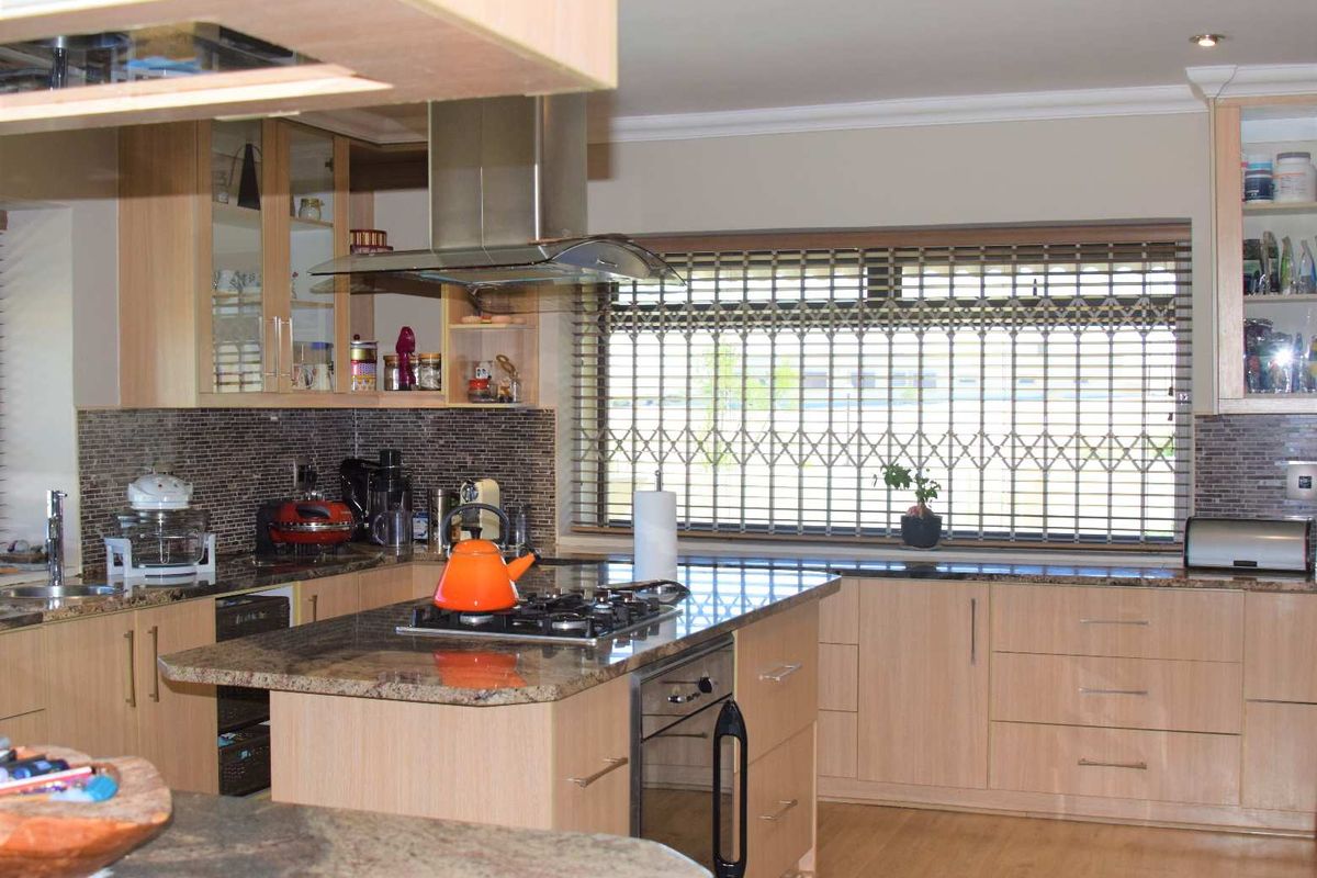 A well-appointed kitchen featuring light wood cabinetry, granite countertops, a central island with a built-in gas hob and oven, and a stainless steel extractor fan.