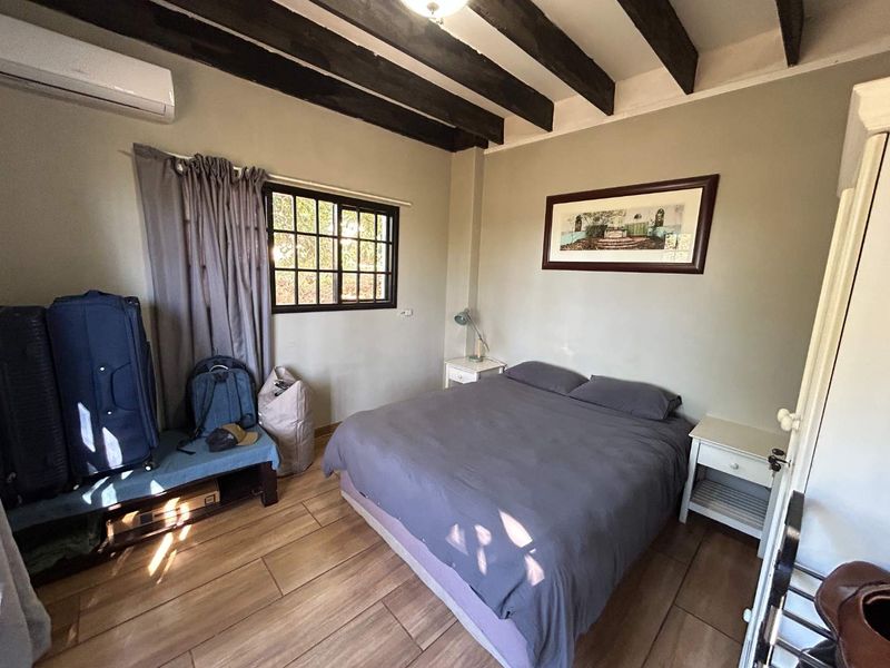 A cozy bedroom featuring exposed timber ceiling beams, tiled flooring, and a wall-mounted split-system air conditioner.