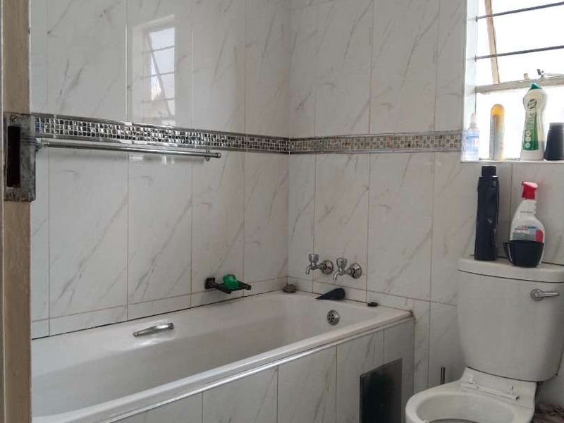 A functional bathroom featuring a bathtub with tiled surround, a toilet, and marble-effect wall tiles with a decorative mosaic border.