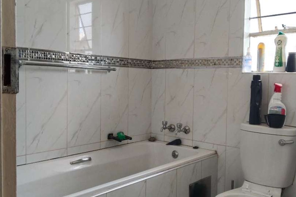 A functional bathroom featuring a bathtub with tiled surround, a toilet, and marble-effect wall tiles with a decorative mosaic border.