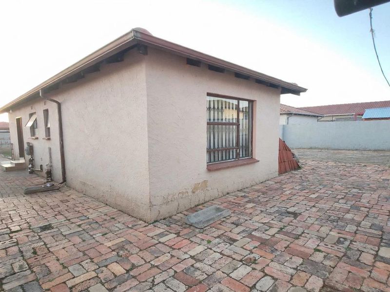 Rear view of the property featuring brick paving, security bars on windows, and a perimeter wall.