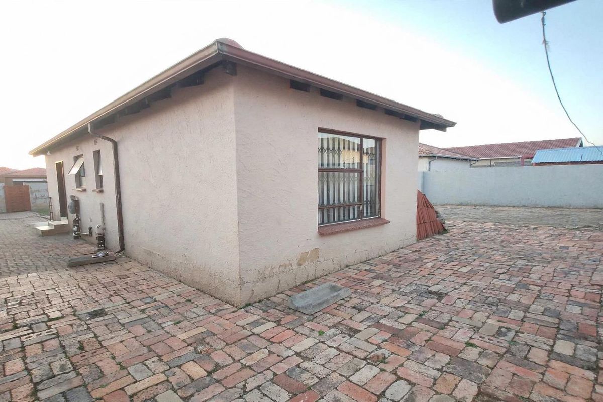 Rear view of the property featuring brick paving, security bars on windows, and a perimeter wall.