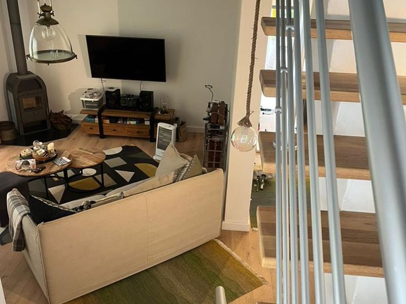 A view from the staircase looking down into a cozy living area featuring a wood-burning stove, timber flooring, and a modern metal balustrade.