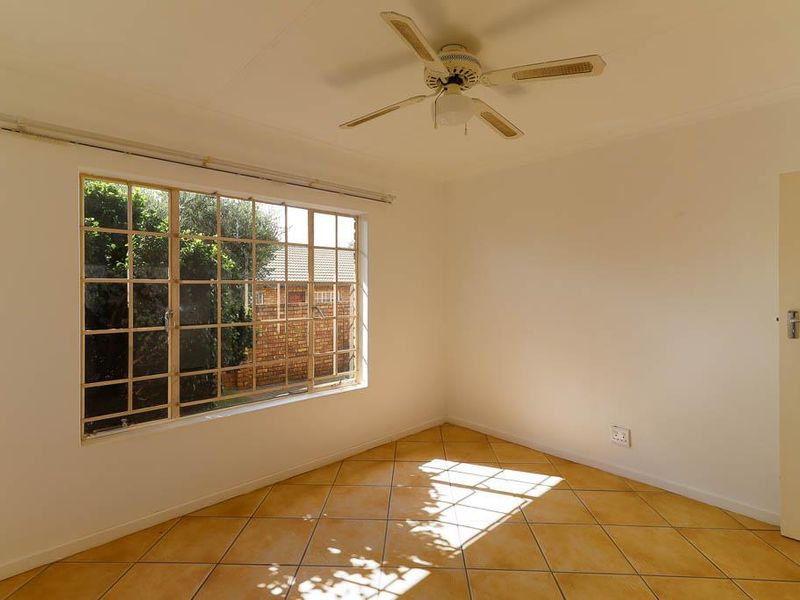 A bright, empty bedroom featuring tiled flooring, a ceiling fan, and a large grid-pattern window overlooking the exterior.