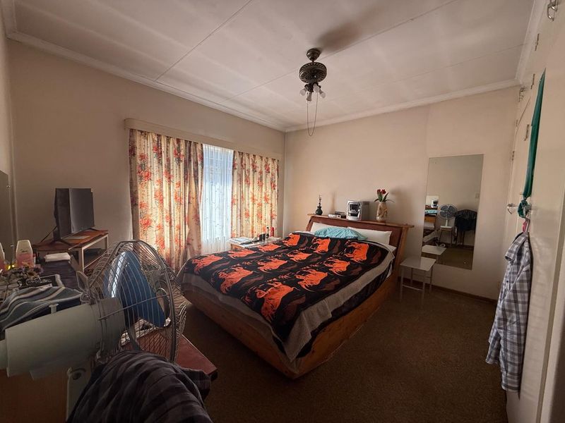 A functional bedroom featuring carpeted flooring, a ceiling fan, and a built-in wall mirror, offering a comfortable and practical living space.
