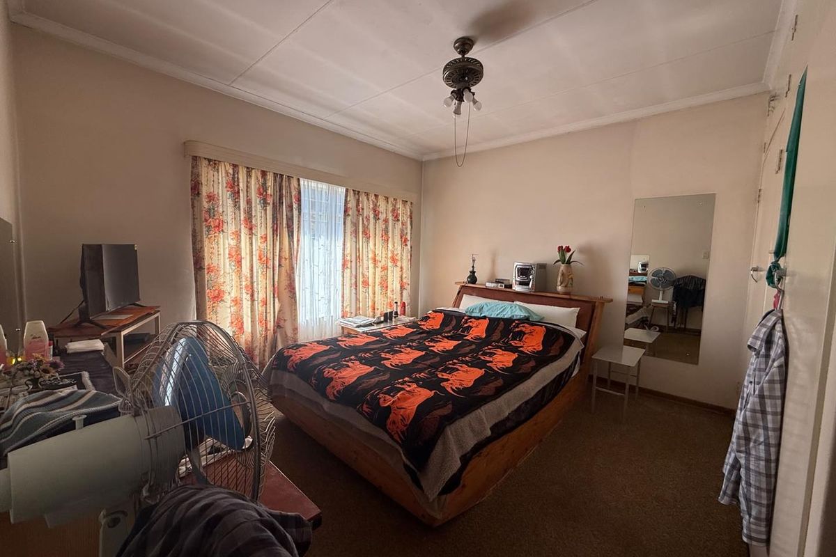A functional bedroom featuring carpeted flooring, a ceiling fan, and a built-in wall mirror, offering a comfortable and practical living space.