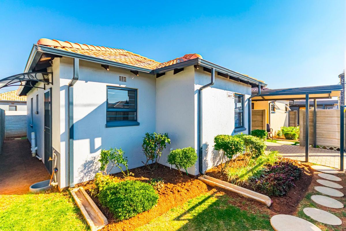 A well-maintained rear exterior view of the house featuring a tiled roof, paved pathways, and a covered carport area.