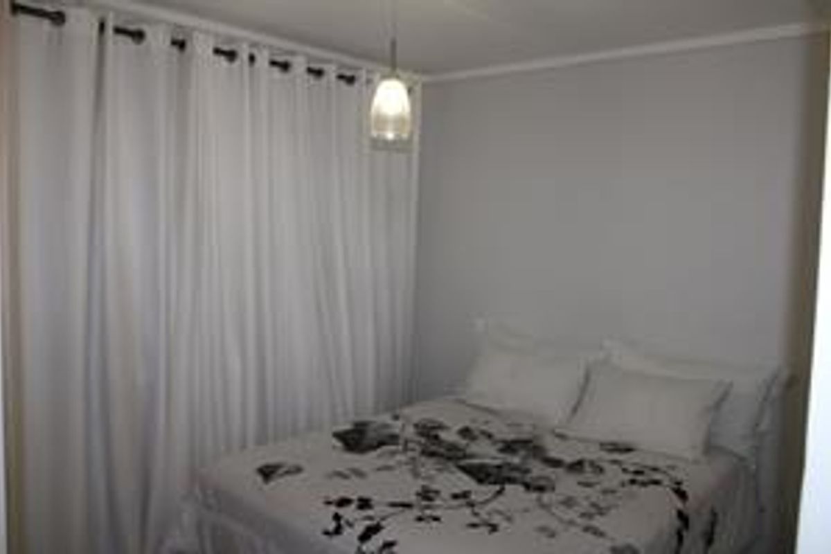 A compact bedroom featuring neutral wall finishes, a pendant light fixture, and floor-to-ceiling curtains.