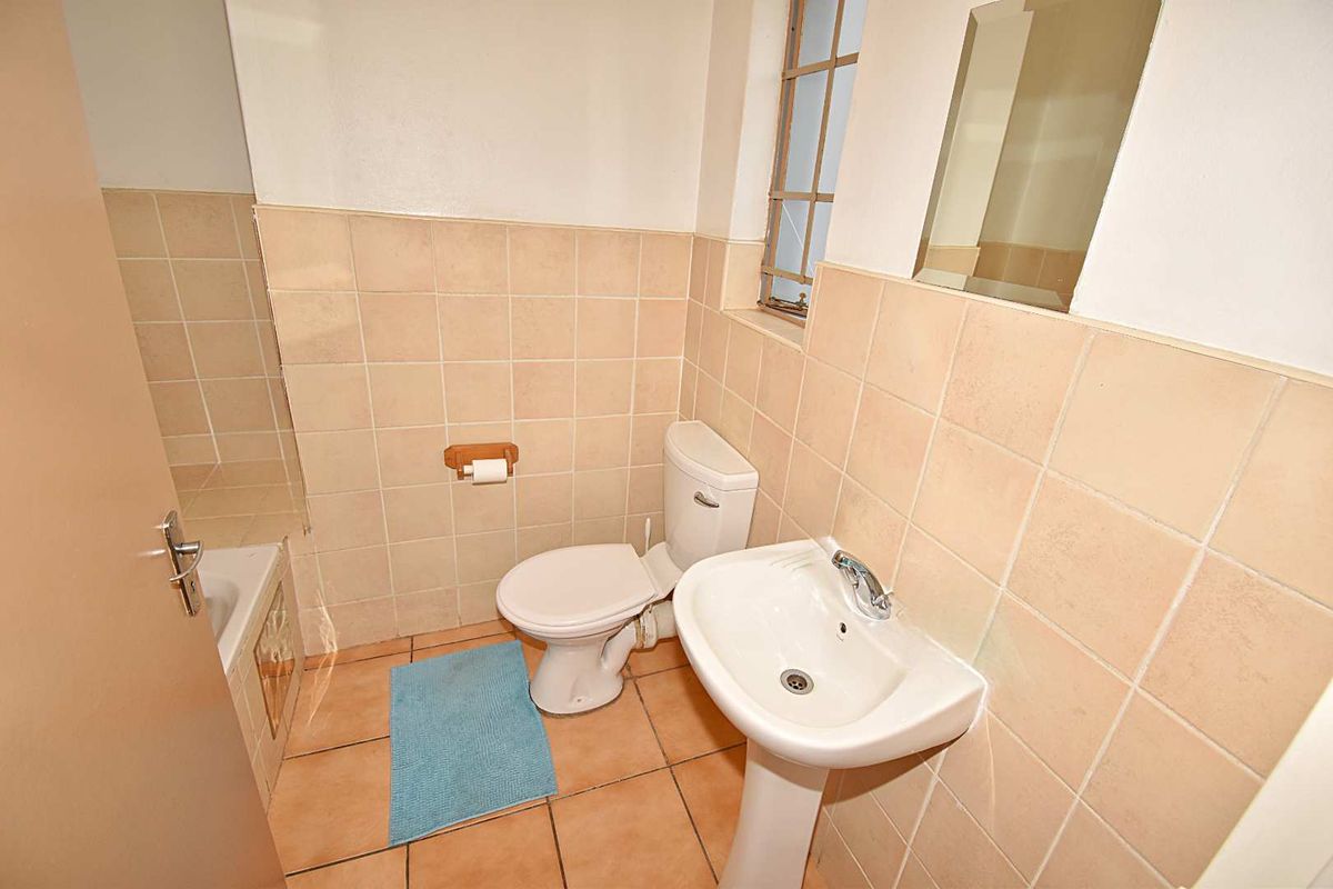 A functional bathroom featuring a pedestal basin, toilet, and bathtub with neutral wall and floor tiling.
