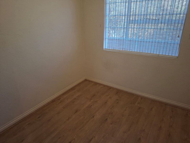 An empty bedroom featuring laminate flooring, neutral walls, and fitted window blinds, offering a clean and versatile space ready for personalization.