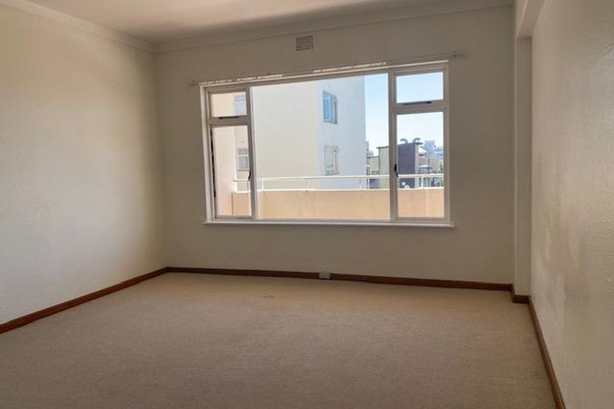 An empty, neutrally painted bedroom featuring large windows with natural light and carpeted flooring, offering a blank canvas for potential interior design updates.