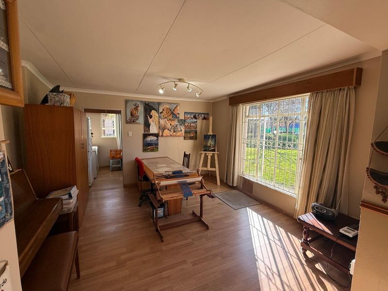 A bright living area featuring laminate flooring, coved ceilings, and a large window with security bars overlooking the garden.