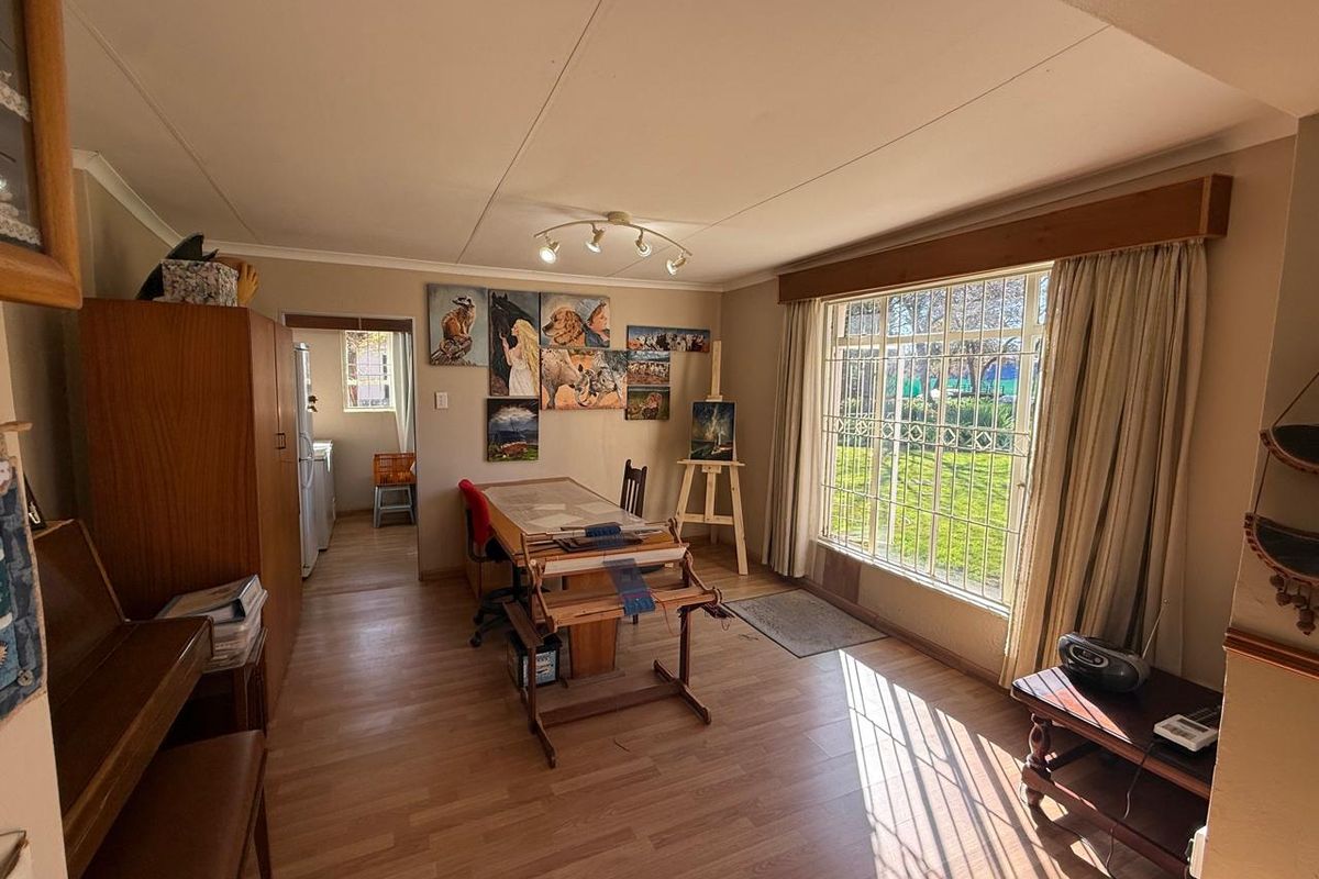 A bright living area featuring laminate flooring, coved ceilings, and a large window with security bars overlooking the garden.