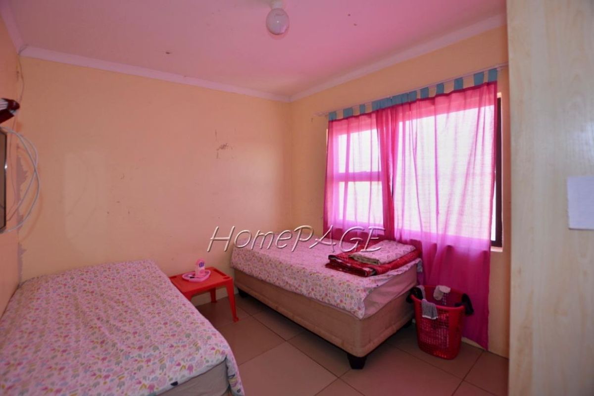 A bedroom featuring tiled flooring and a window with pink curtains, providing a functional space for rest.