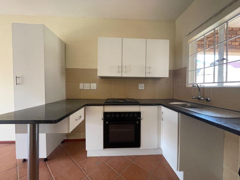 A functional kitchen featuring white cabinetry, black granite countertops, a built-in oven and hob, and tiled flooring with a window overlooking the exterior.