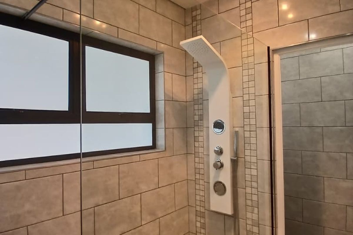 Modern walk-in shower featuring a contemporary shower panel, glass screen, and neutral subway wall tiling with mosaic floor accents.