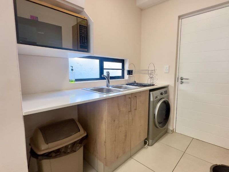 A functional laundry area featuring built-in cabinetry, a stainless steel sink, tiled flooring, and space for a washing machine.