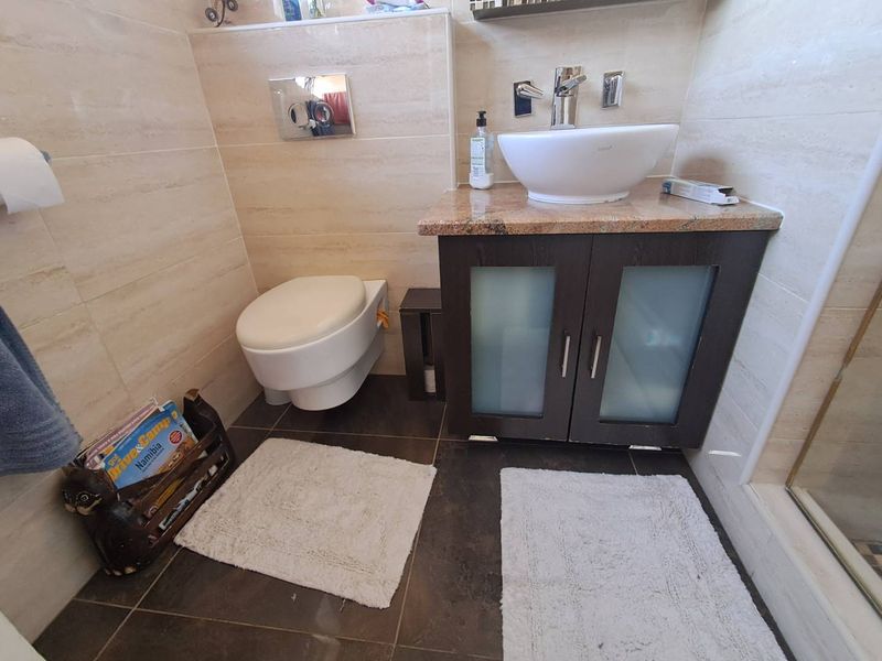 A compact bathroom featuring a wall-mounted toilet, a dark wood vanity cabinet with a granite countertop, and a modern vessel sink.