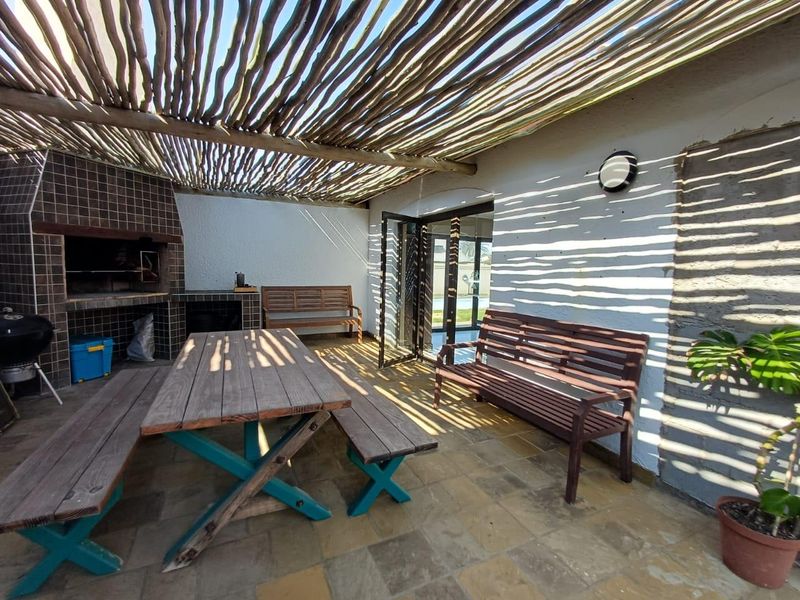 Covered outdoor patio area featuring a built-in braai, rustic pergola roof, and tiled flooring, ideal for alfresco dining and entertaining.