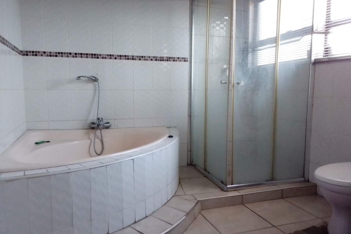 A dated bathroom featuring a corner bathtub, separate shower enclosure, and tiled finishes, offering potential for a modern renovation.