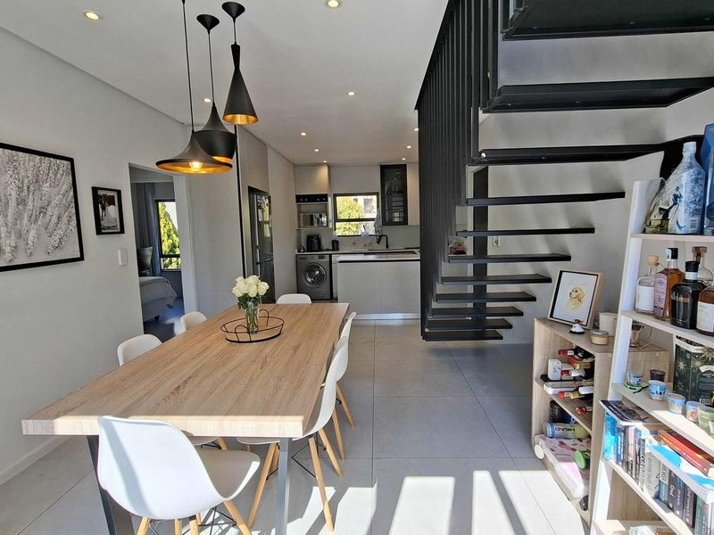 Modern open-plan living and dining area featuring tiled floors, recessed lighting, and a striking open-tread staircase leading to the upper level.