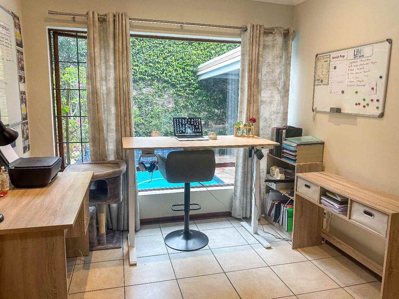 A functional home office space featuring tiled flooring and a large window overlooking the garden and pool area.