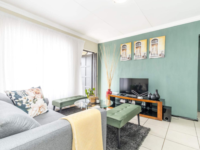 A bright and well-maintained living room featuring neutral tiled flooring, decorative cornicing, and a sliding door providing access to the exterior.