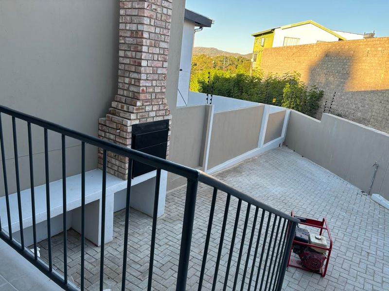 Outdoor patio area featuring a built-in brick braai, concrete counter, and paved flooring, enclosed by a perimeter wall with electric fencing.