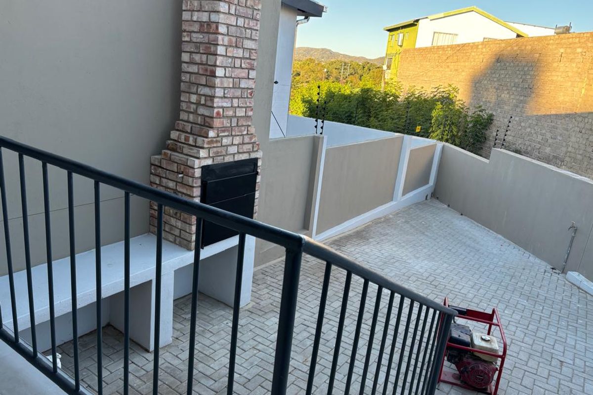 Outdoor patio area featuring a built-in brick braai, concrete counter, and paved flooring, enclosed by a perimeter wall with electric fencing.