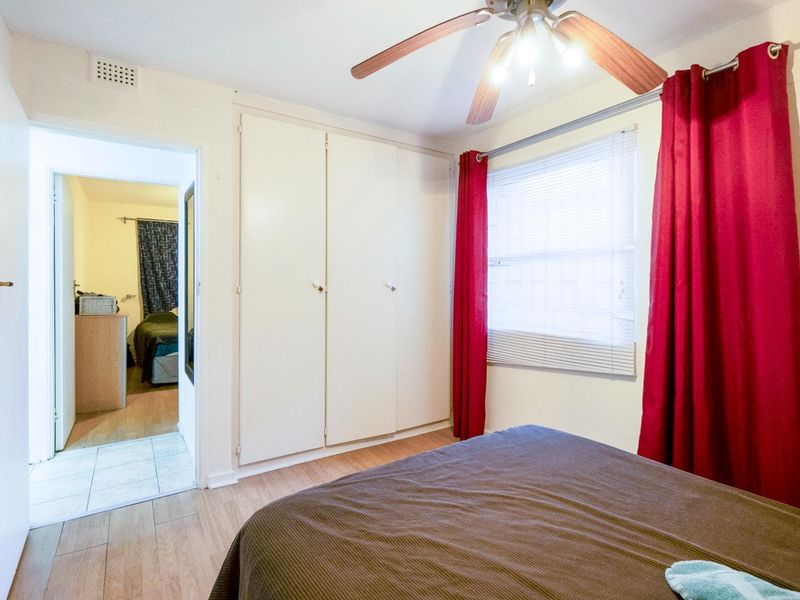 A bedroom featuring built-in wardrobes, a ceiling fan, and laminate flooring, with an adjacent view into another room.