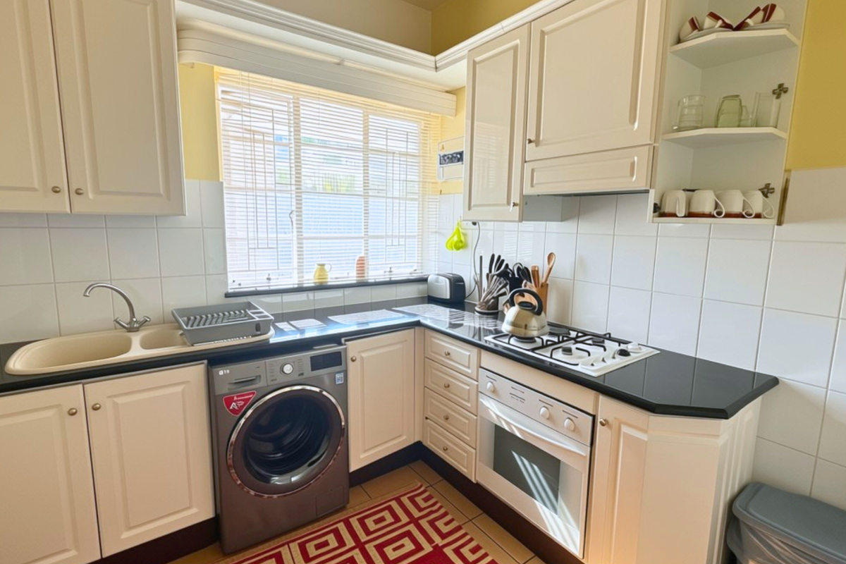 A functional kitchen featuring cream cabinetry, black granite countertops, a gas hob, built-in oven, and a double basin sink with tiled splashbacks.
