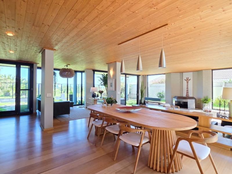 Spacious open-plan living and dining area featuring warm timber ceilings, polished wood flooring, a built-in fireplace, and expansive sliding glass doors leading outdoors.