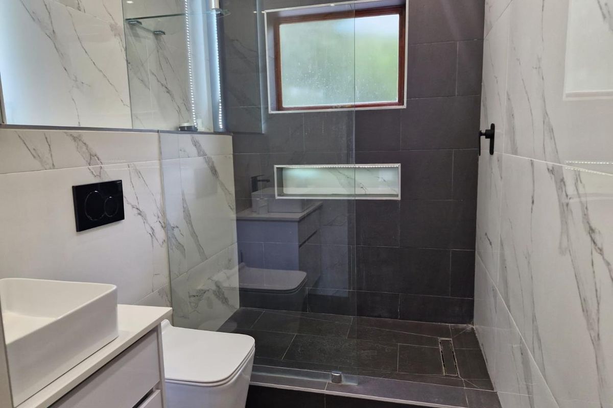Modern bathroom featuring a walk-in shower with glass screen, dark tiled walls, marble-effect wall tiles, and a contemporary vanity unit.